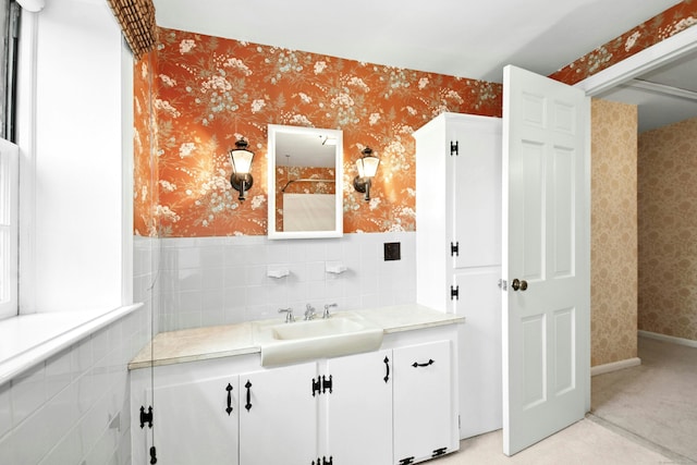 bathroom featuring wallpapered walls, wainscoting, vanity, and tile walls