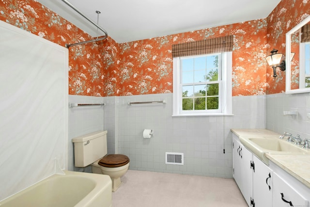 full bath featuring wallpapered walls, tile walls, wainscoting, toilet, and a tub