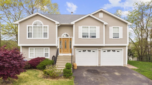 split foyer home featuring a garage, a shingled roof, and driveway