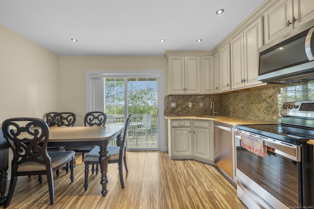 kitchen featuring stainless steel appliances, a sink, cream cabinetry, backsplash, and light wood-type flooring