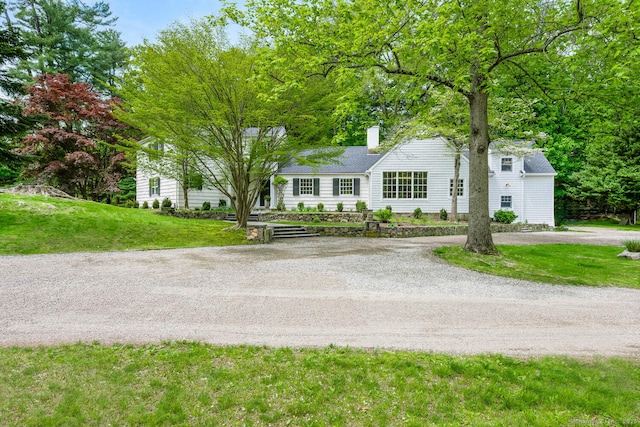 view of front of home with dirt driveway, a front yard, and a chimney