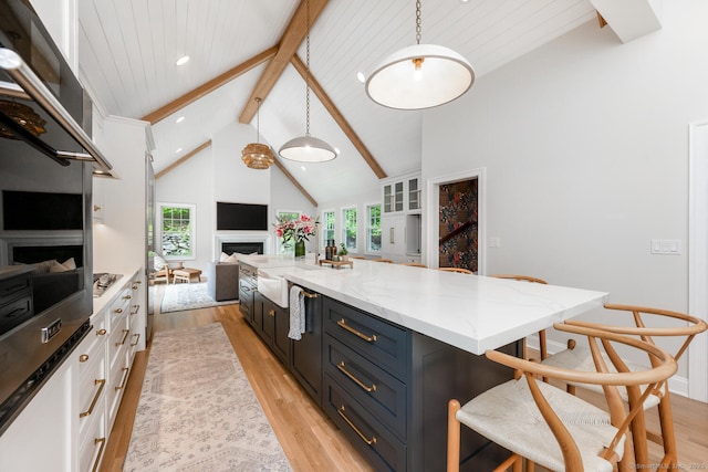kitchen featuring beam ceiling, light wood-type flooring, a fireplace, white cabinets, and light stone countertops