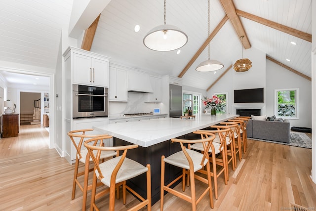 kitchen featuring appliances with stainless steel finishes, custom exhaust hood, white cabinetry, beamed ceiling, and light wood-type flooring