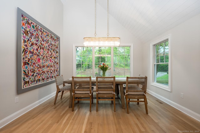 dining room featuring light wood-style floors, a chandelier, baseboards, and high vaulted ceiling