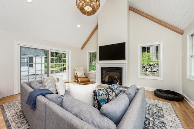 living area featuring beamed ceiling, wood finished floors, a fireplace with flush hearth, high vaulted ceiling, and baseboards
