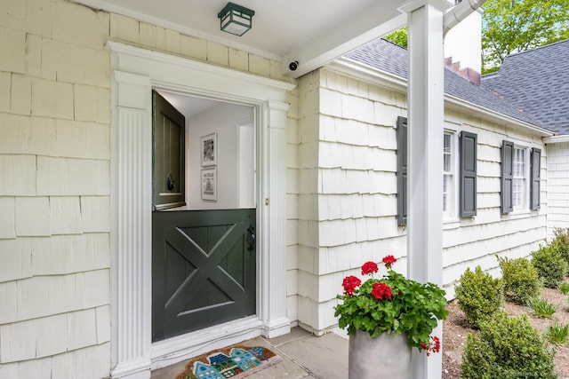 view of exterior entry with a security system and a shingled roof
