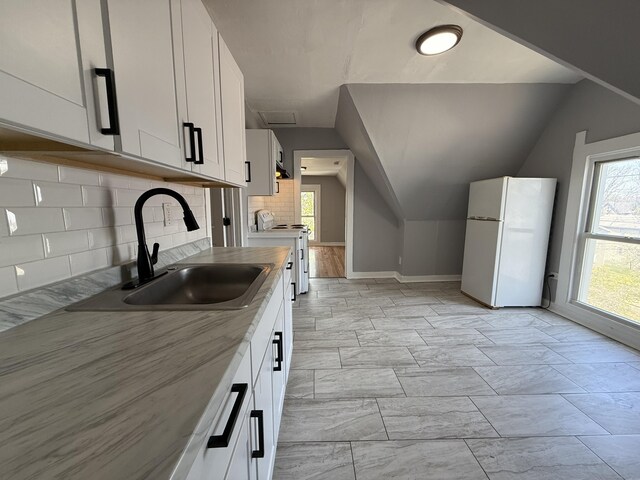 kitchen featuring white appliances, a sink, white cabinets, tasteful backsplash, and baseboards