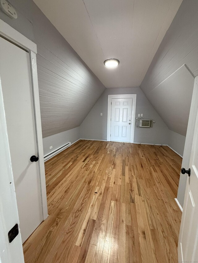 bonus room with baseboard heating, hardwood / wood-style floors, vaulted ceiling, and a wall unit AC