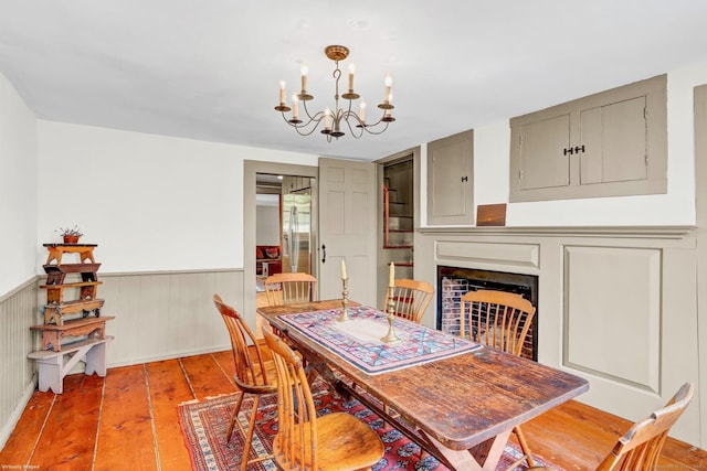 dining area featuring a notable chandelier, hardwood / wood-style floors, a fireplace, and a wainscoted wall