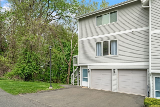 view of property exterior featuring a yard, driveway, a garage, and stairs