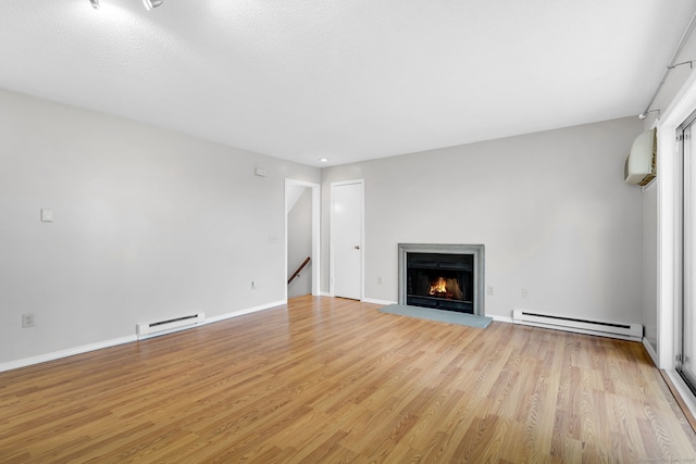 unfurnished living room featuring a baseboard heating unit, a warm lit fireplace, light wood finished floors, and an AC wall unit
