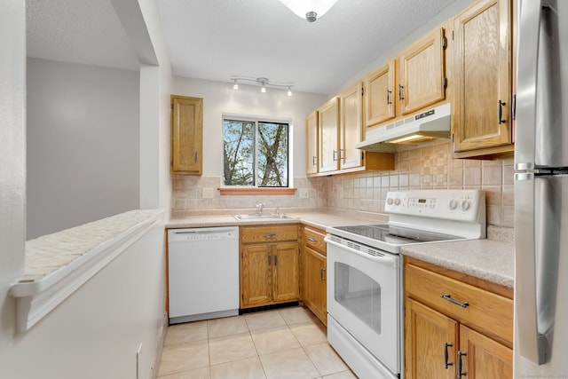 kitchen with light tile patterned floors, a sink, white appliances, under cabinet range hood, and light countertops