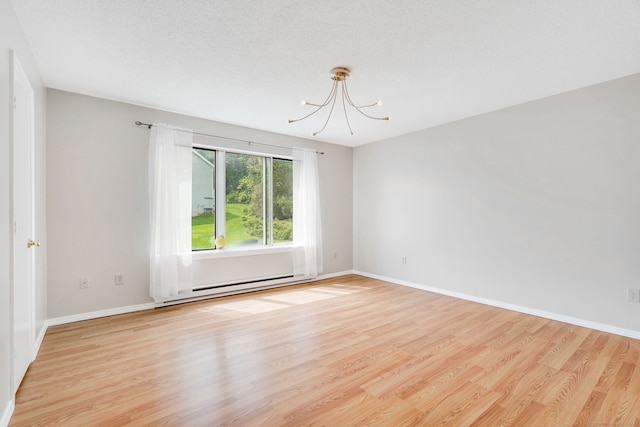 empty room featuring a chandelier, light wood-style flooring, baseboards, and a baseboard heating unit