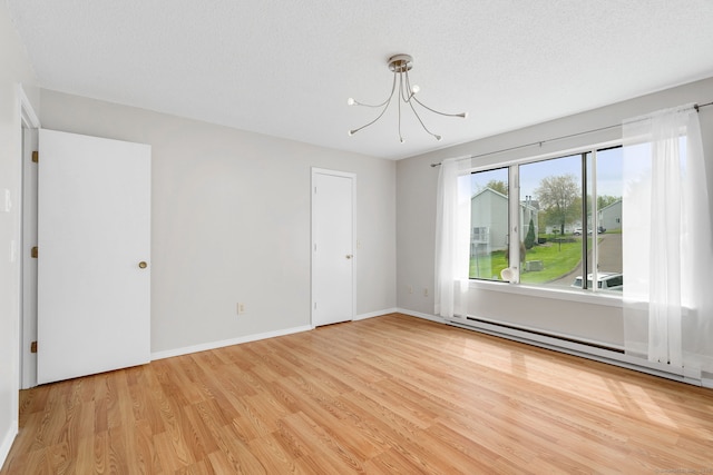 empty room with baseboards, baseboard heating, light wood-style flooring, and a chandelier