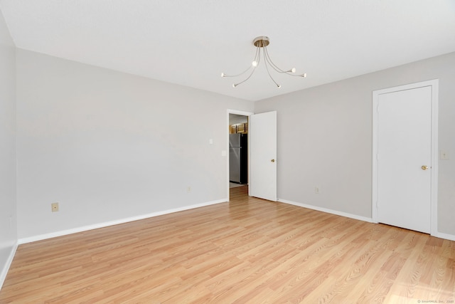 unfurnished room with baseboards, a notable chandelier, and light wood-style flooring