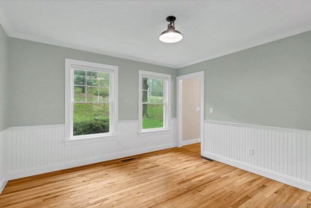 unfurnished room featuring wood finished floors, wainscoting, and crown molding