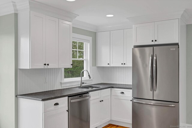 kitchen featuring appliances with stainless steel finishes, a sink, dark countertops, white cabinets, and crown molding