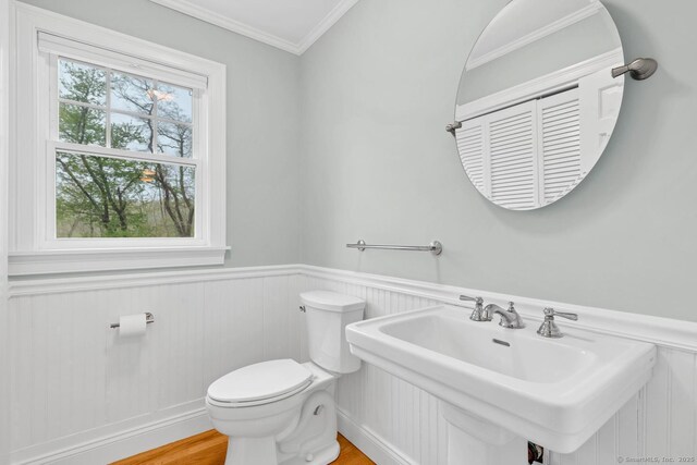 bathroom with a sink, toilet, a wainscoted wall, ornamental molding, and wood finished floors