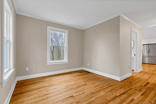 empty room with light wood-style flooring, ornamental molding, and baseboards