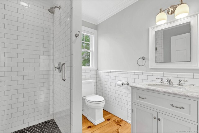 full bathroom featuring crown molding, a stall shower, toilet, a wainscoted wall, and tile walls