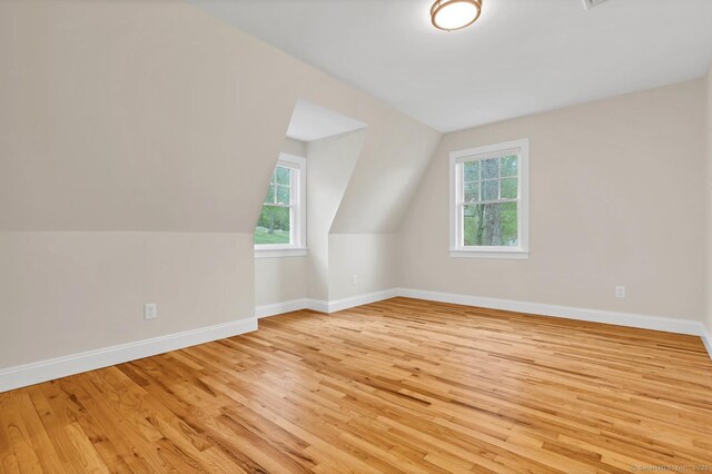 bonus room featuring healthy amount of natural light, light wood finished floors, vaulted ceiling, and baseboards