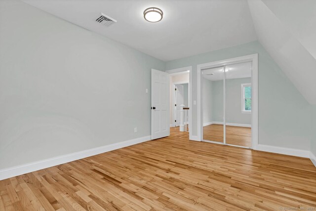 unfurnished bedroom with light wood finished floors, baseboards, a closet, and vaulted ceiling