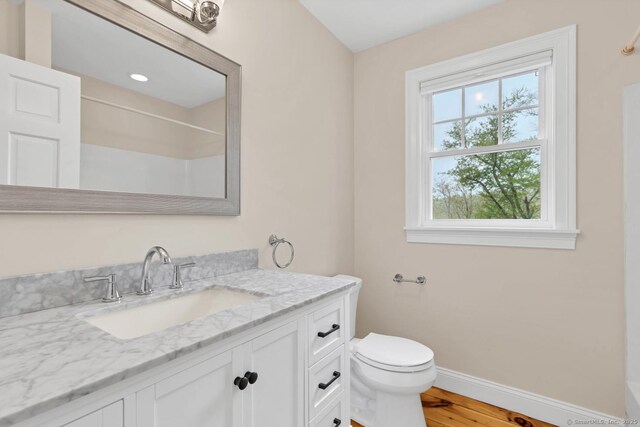 bathroom with baseboards, toilet, vanity, wood finished floors, and a shower