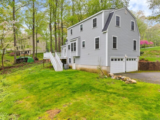 rear view of house with asphalt driveway, stairs, a garage, a lawn, and a wooden deck