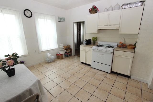 kitchen with white gas stove, under cabinet range hood, light countertops, white cabinets, and light tile patterned floors