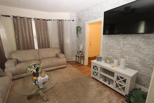 living room featuring brick wall, wood finished floors, and a ceiling fan