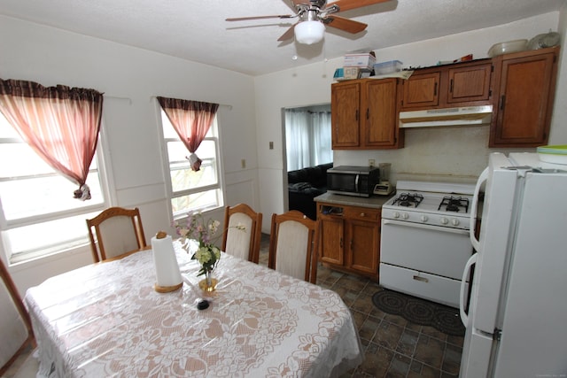 kitchen with white appliances, under cabinet range hood, brown cabinets, and a ceiling fan