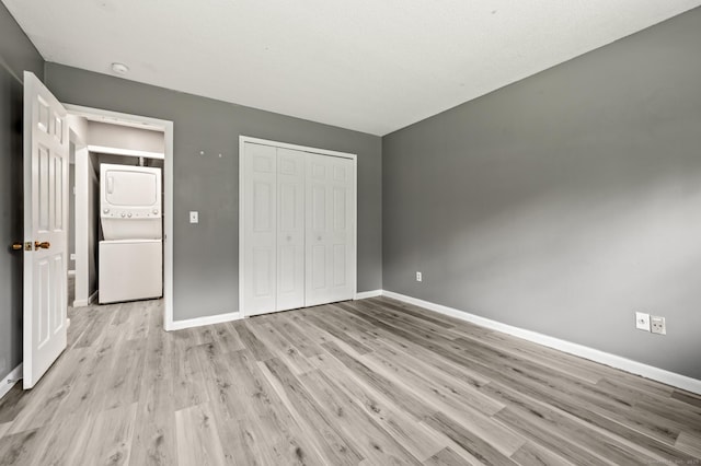 unfurnished bedroom with estacked washer and dryer, baseboards, light wood-style flooring, and a closet