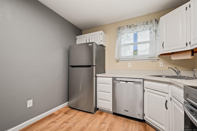 kitchen featuring appliances with stainless steel finishes, a sink, white cabinets, and light wood-type flooring