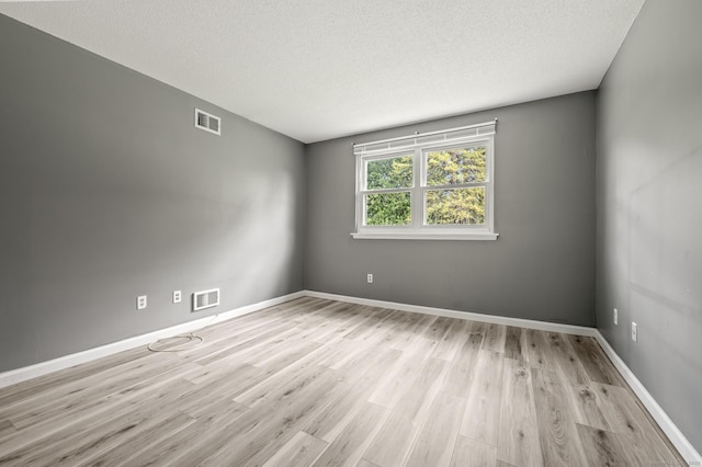 empty room with light wood finished floors, a textured ceiling, and baseboards