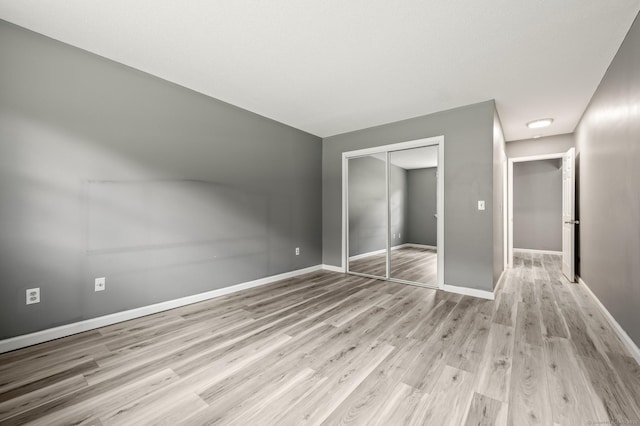 unfurnished bedroom with a closet, light wood finished floors, and baseboards