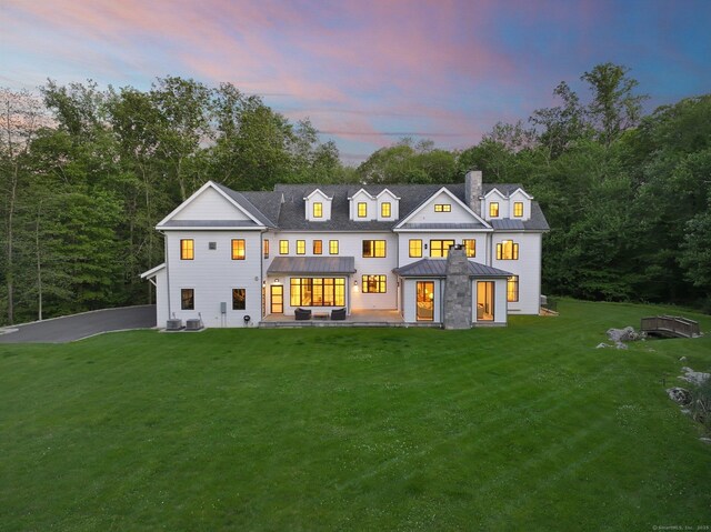 168 Proprietors Xing, New Canaan, CT 06840 - back of property at dusk with a chimney, a standing seam roof, a yard, and metal roof