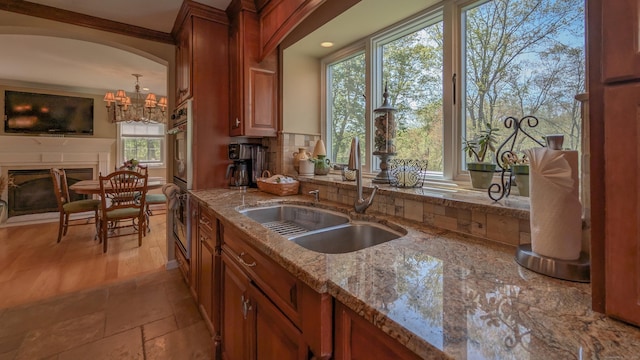 230 Ball Pond Rd, New Fairfield, CT 06812 - kitchen featuring light stone counters, a sink, a chandelier, backsplash, and brown cabinets