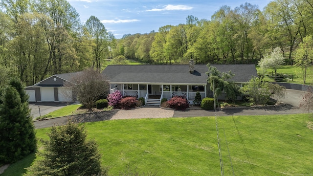 back of house with covered porch, a yard, a chimney, driveway, and a view of trees