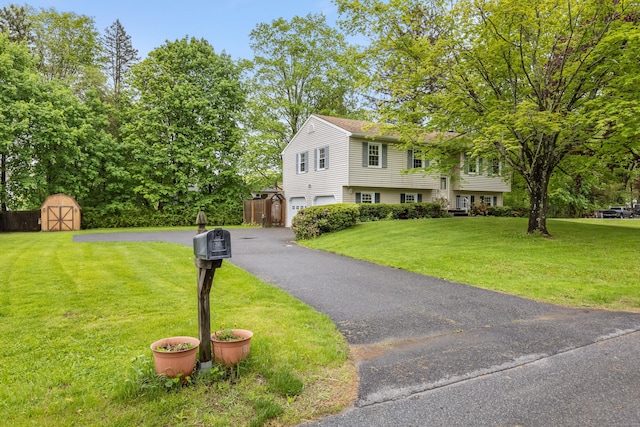 bi-level home featuring a shed, a garage, asphalt driveway, a front yard, and an outbuilding