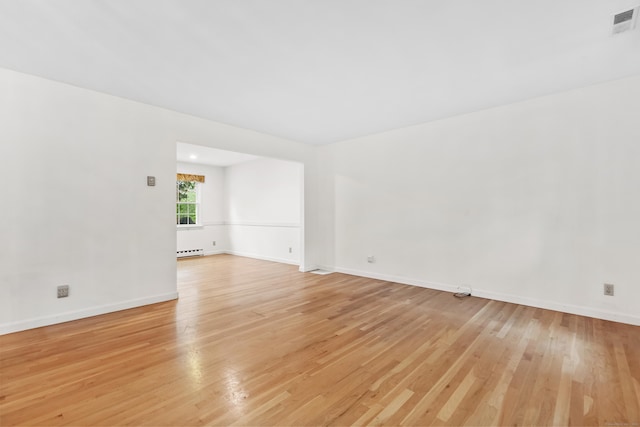 empty room featuring light wood finished floors, baseboard heating, and baseboards