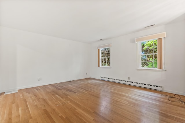 spare room with a baseboard radiator, light wood finished floors, and baseboards
