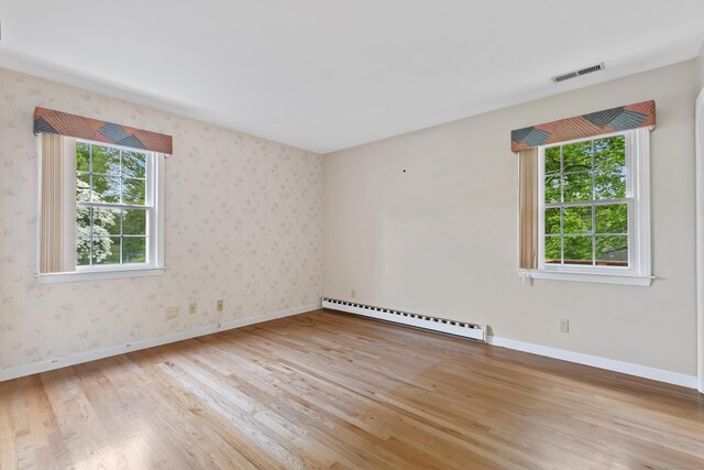 unfurnished room with baseboard heating, healthy amount of natural light, wood finished floors, baseboards, and wallpapered walls