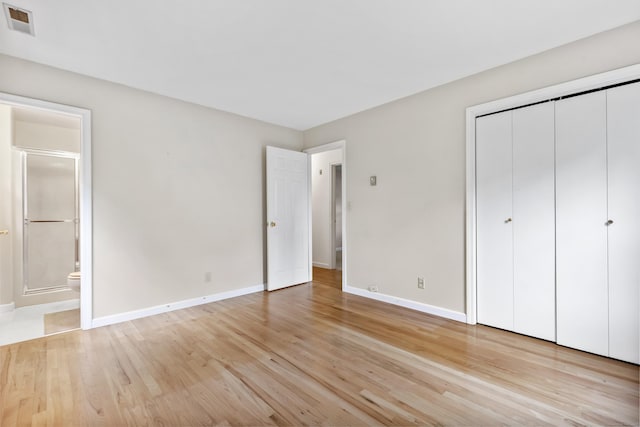 unfurnished bedroom featuring baseboards, light wood-style floors, a closet, and ensuite bath