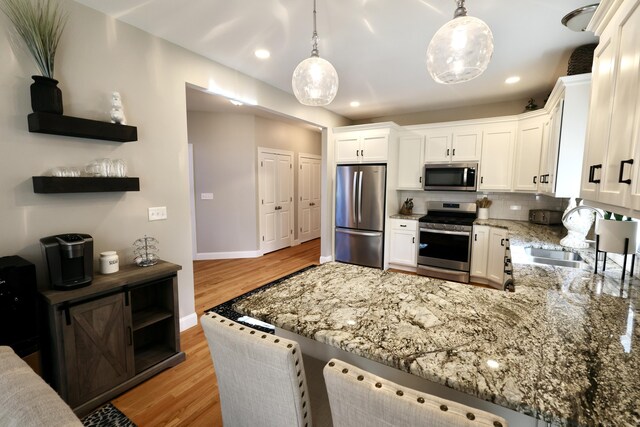 kitchen with appliances with stainless steel finishes, a sink, light stone countertops, white cabinets, and light wood-style flooring