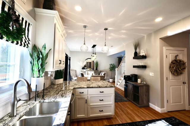 kitchen with a sink, a peninsula, white cabinetry, dark wood finished floors, and hanging light fixtures