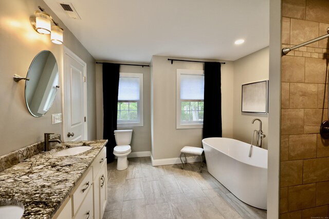 bathroom featuring a freestanding tub, baseboards, double vanity, toilet, and a tile shower