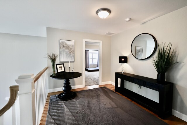 hall with wood finished floors, baseboards, and an upstairs landing