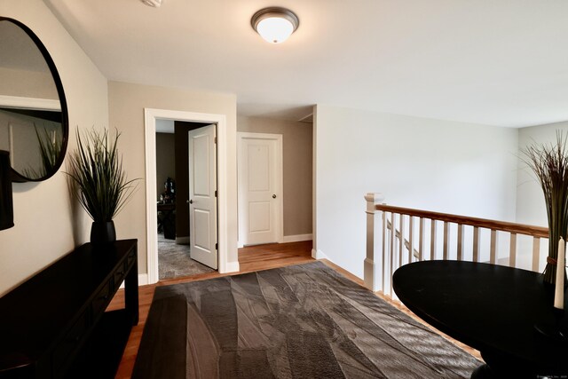 hall with baseboards, wood finished floors, and an upstairs landing