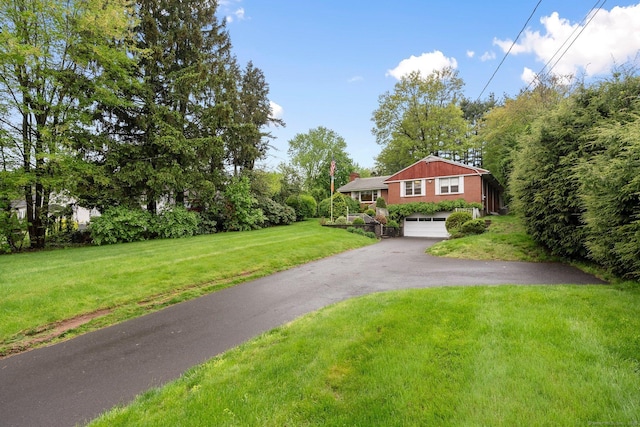 view of front of home featuring asphalt driveway, a garage, a front lawn, and a chimney