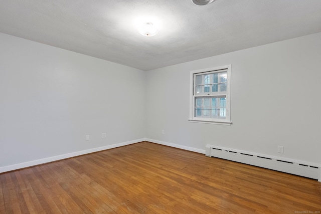 spare room featuring a baseboard radiator, wood finished floors, and baseboards